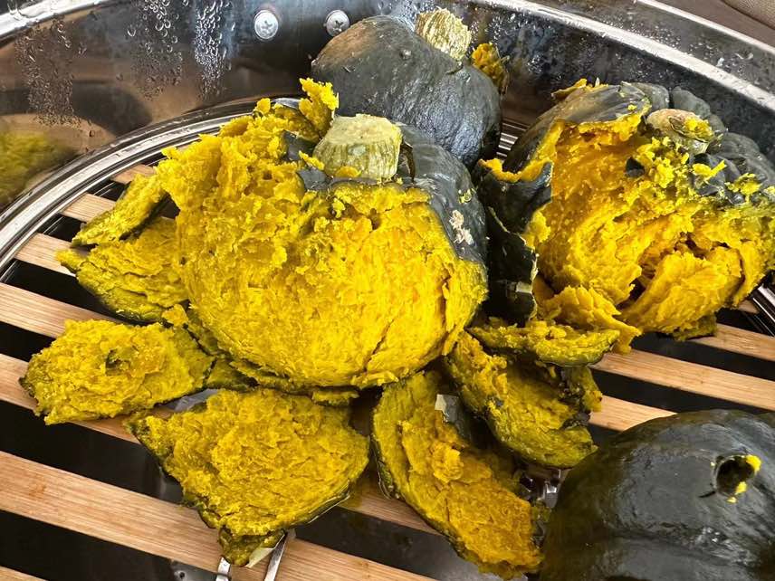 两颗完整蒸熟的贝贝南瓜被对半切开放置在白色瓷盘中,瓜肉呈金黄色,冒着微微热气,旁边搭配一小撮黑芝麻和薄荷叶装饰,展现健康美味的家常料理风格 蒸熟后的贝贝南瓜摆盘美食图