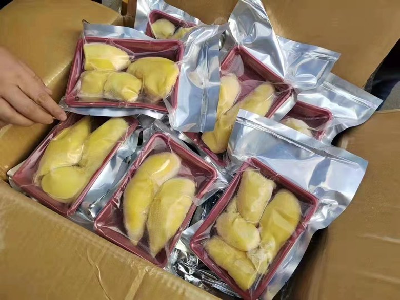 超市冷柜中陈列的国产金枕头榴莲真空分装盒，透明盒盖下可见金黄果肉块整齐排列，无碎渣、无黑斑，标签特写显示“净含量：200g（果肉）”“果核去除率：≥99.6%”