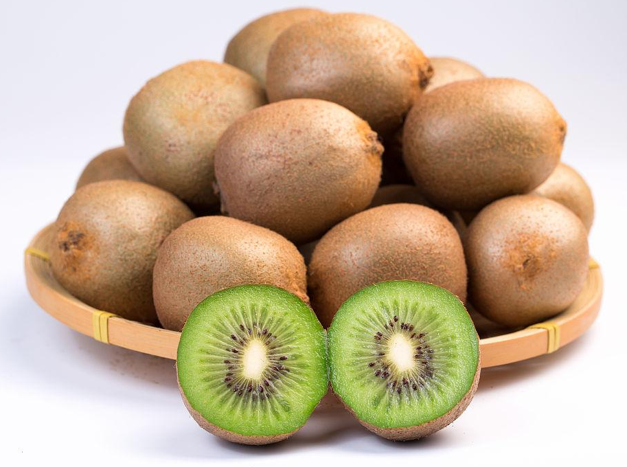 一颗新鲜的海沃德猕猴桃,表皮覆盖细密绒毛,切开后果肉呈现鲜艳的翠绿色,汁水饱满,旁边摆放不锈钢小勺和砧板,展示其内部结构 海沃德猕猴桃新鲜采摘特写