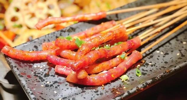 一盘色泽鲜亮、香气扑鼻的麻辣烤串烤尖椒,摆放在木质托盘上,辣椒表面微微焦香,撒满辣椒粉和芝麻,旁边是几根签子,背景为烧烤摊夜市氛围 烤尖椒特写图