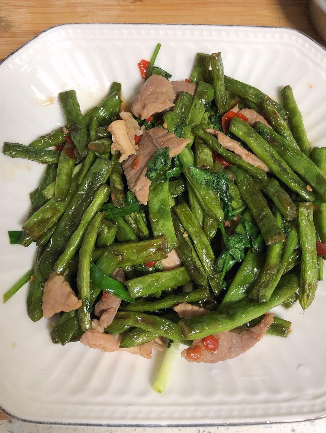 一盘刚出锅的四季豆猪肉馅饺子整齐摆放在白色瓷盘中,饺子皮晶莹透亮,隐约可见绿色馅料,表面泛着油光,旁边点缀香菜和红辣椒圈,背景为家庭餐桌温馨场景 四季豆饺子成品图