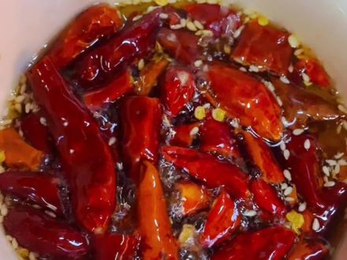 厨师正在将热油缓缓倒入装有辣椒碎和芝麻的陶瓷碗中，油花翻滚，香气四溢