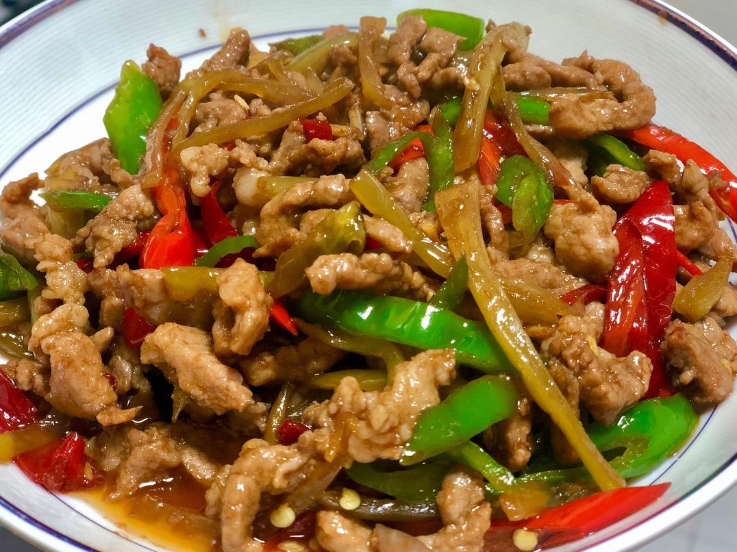 一盘刚出锅的辣椒炒肉特写,红绿鲜椒与棕褐色肉片交织,表面泛着油光,背景虚化的米饭冒着热气,营造出诱人的家常美食氛围 成品菜肴展示图