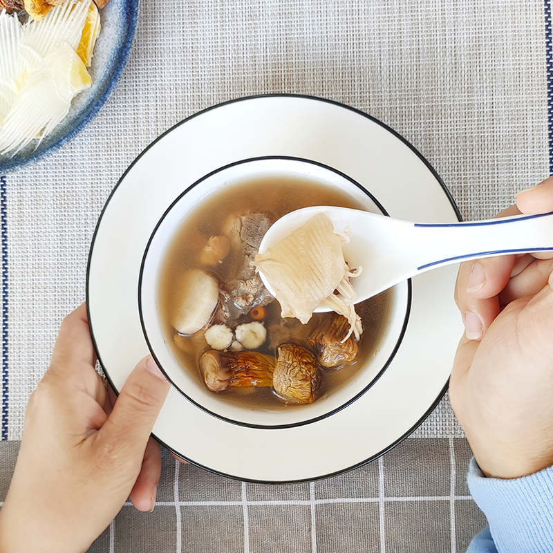 生活化场景图:厨房操作台上摆放已泡发的鱼胶、生晒参片、红枣、枸杞等食材,一位中年女性正在将材料放入白色瓷炖盅,背后为电炖锅工作状态,光线柔和,体现家庭健康烹饪的真实情境 鱼胶炖洋参家庭炖煮过程场景