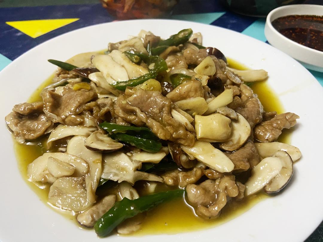 一道装在白色瓷盘中的干香菇炒五花肉,香菇片油亮饱满,五花肉呈琥珀色,表面微焦,青蒜翠绿点缀其上,整体冒着热气,背景虚化的木质餐桌 成品干香菇炒五花肉特写图