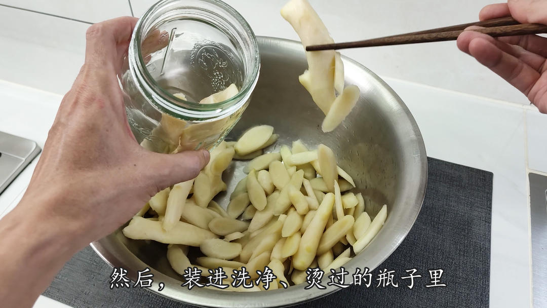 一位家庭主妇正在玻璃罐中放入切片子姜,准备制作醋泡姜 家庭厨房中的醋泡姜制作场景