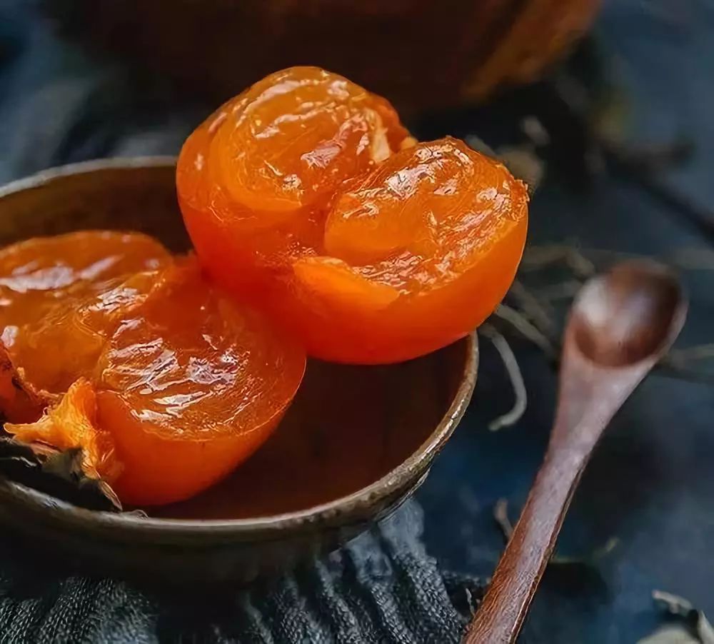 一颗完全成熟的橙红色柿子被横向切开,露出晶莹透亮的果肉,汁水微微渗出,果核清晰可见,背景为白色陶瓷盘,光线聚焦于切面中心,展现细腻果肉纹理 成熟柿子切面特写