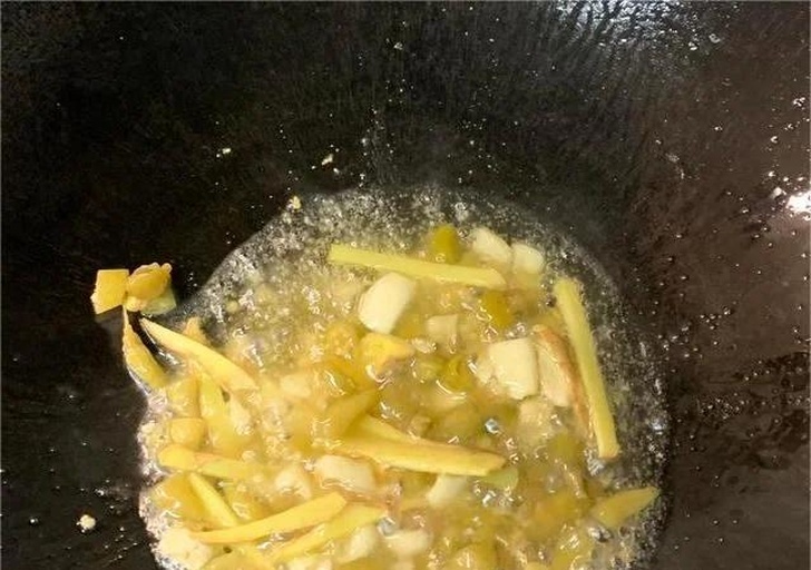 铸铁炒锅内正在翻炒姜片、蒜瓣和葱段,油面泛起金黄气泡,散发浓郁香气,背景虚化显示灶具环境 锅中爆香调料特写