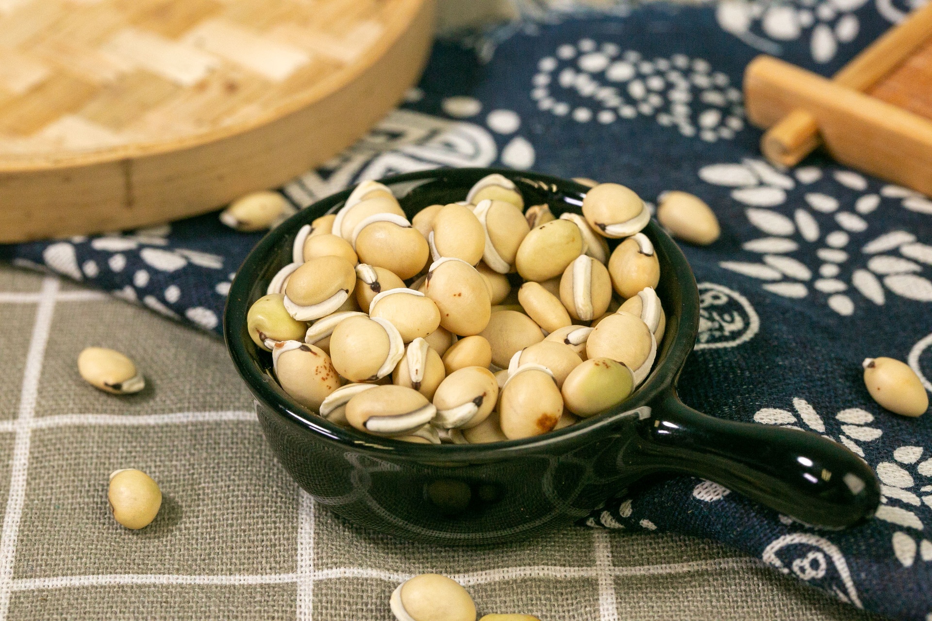 一位中年女性在厨房中正在将泡发后的蚕豆倒入锅中与大米一同熬煮,灶台上摆放着葱姜调料,环境整洁温馨,体现家常健康饮食氛围 家庭烹饪蚕豆场景