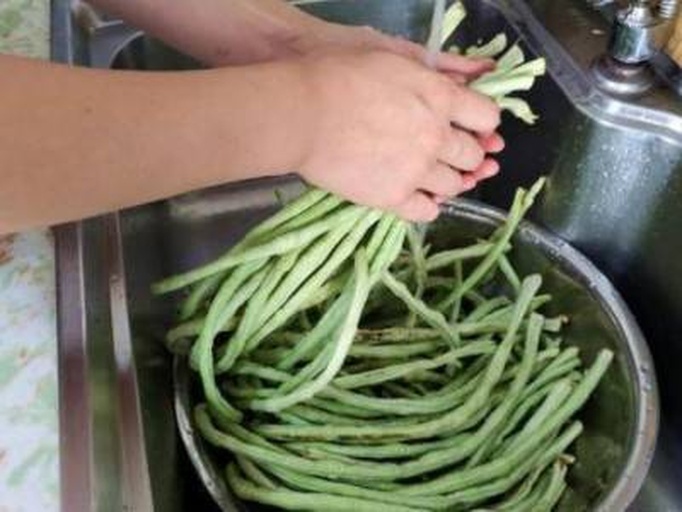 一位厨师正在水槽中清洗新鲜的荷兰豆,背景为现代化厨房环境 荷兰豆在厨房中清洗的场景