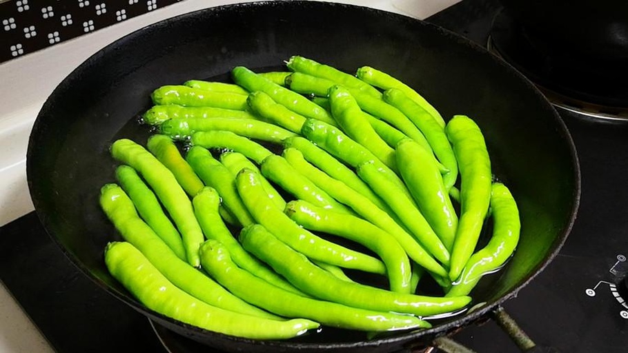 一位家庭主妇正在现代化厨房中用铁锅翻炒切好的青椒和彩色圆椒,锅中菜肴色泽鲜亮,冒着热气,旁边案板上放着剩余的圆椒和调味料,整体画面温馨且富有生活气息 家庭厨房中正在炒制青椒圆椒菜肴