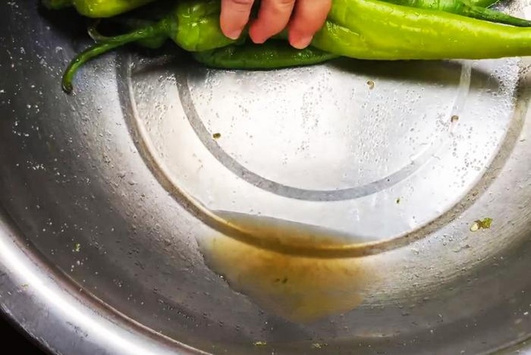 一位厨师在厨房水槽中用手清洗一根长条形青茄子,水流冲刷着光亮的表皮,旁边放置菜板和刀具,背景可见有机标签的蔬菜包装袋 厨房中正在清洗青茄子的过程