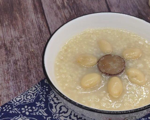 微距特写:陶锅中温热的豆角豆乳粥,豇豆丁已炖至软糯呈浅橄榄绿,豆浆形成柔滑米白色基底,表面浮着细小豆油星,撒有少许葱花,体现温和易消化的烹饪转化 豆角豆乳粥特写图