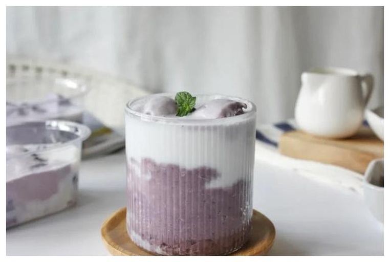 透明塑料杯中分层展示紫薯芋泥与牛奶,上层为浅紫色顺滑泥状物,下层为乳白色液体,杯壁附着黑色波波珍珠,置于木质托盘上,背景虚化的甜品柜台显示‘芋泥系列’字样 甜品店中的紫薯芋泥杯