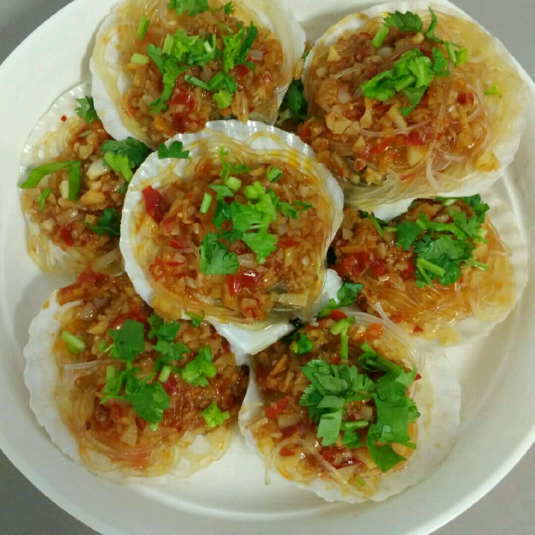 一盘刚出锅的白胡椒蒸扇贝,贝壳洁白,扇贝肉饱满呈乳白色,表面覆盖金黄蒜蓉酱汁,点缀绿色葱花,蒸汽袅袅升起,展现极致鲜美感 蒸扇贝成品特写