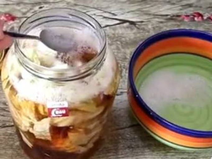 一个透明玻璃发酵罐中装有半满的青提混合物,液体呈淡黄绿色,表面有细密气泡不断上升,罐口连接着水封阀,装置放置在木质桌面上,背景为昏暗储藏室 青提发酵罐