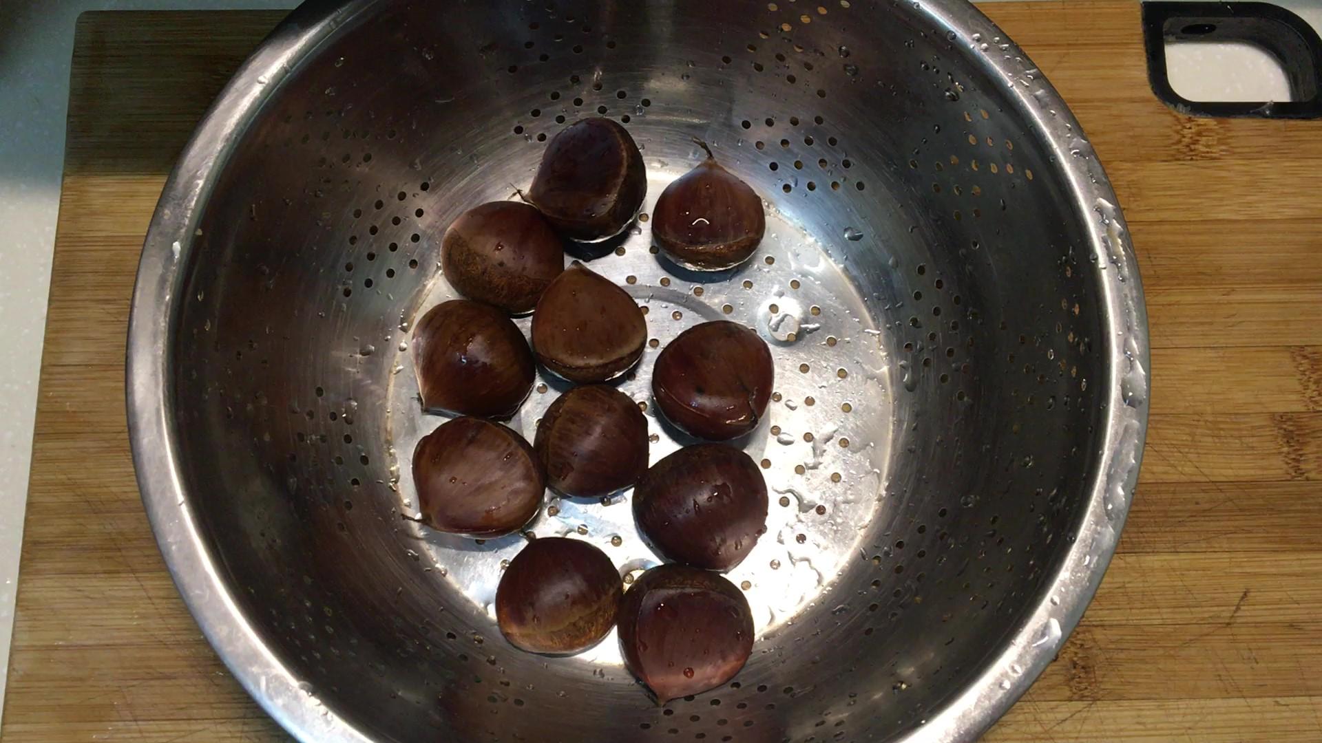 一位家庭主妇正在厨房用不锈钢蒸锅蒸煮带缝裂口的生栗子,旁边放着竹制碗碟和新鲜香葱,体现健康家常饮食氛围 家庭厨房中蒸煮栗子的场景