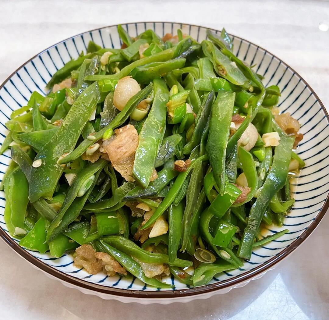 俯拍高清成品图:深褐色五花肉块与油亮墨绿色四季豆交错铺陈于青花瓷浅盘中,表面点缀翠绿葱花与红椒丝,汤汁浓稠挂勺,可见细密油星与微微反光 四季豆炖五花肉成品摆盘