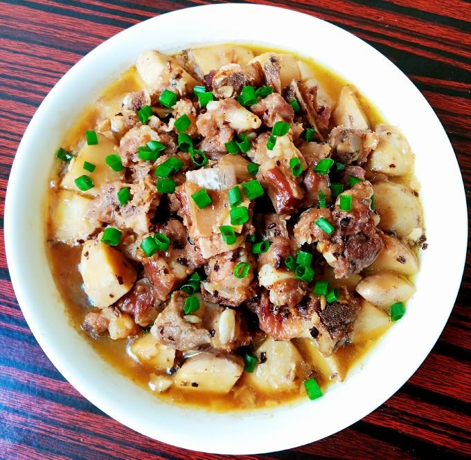 毛芋头炖肉成品图:色泽红亮、汤汁浓稠、搭配米饭的餐桌实拍场景 深褐色浓汁包裹着五花肉与毛芋头的特写镜头,菜肴盛于粗陶碗中,旁边配有米饭和青菜,氛围温暖诱人