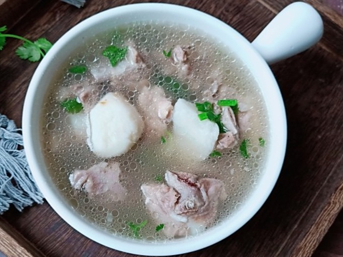 一口砂锅中正炖煮着乳白色的萝卜排骨汤,表面浮有少许油花,可见清晰的白萝卜块和骨头,汤面微微冒泡,旁边摆放着姜片和葱段,整体呈现温暖诱人的家常菜视觉效果 炖煮中的白萝卜汤品