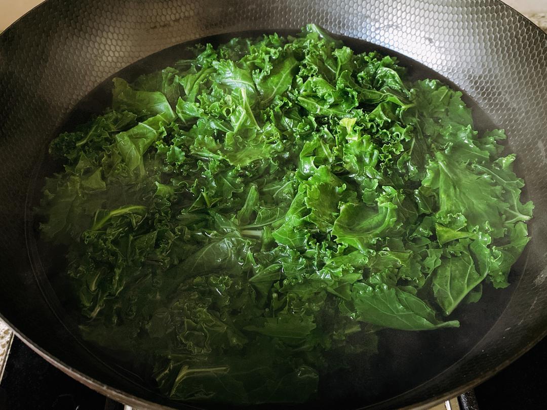 案板上摆放着去皮后的羽衣甘蓝茎,旁边有切片、切丝的不同形态,锅中正在焯水处理,工具包括刀具、刨皮器和不锈钢锅 羽衣甘蓝茎部切片与烹饪过程图