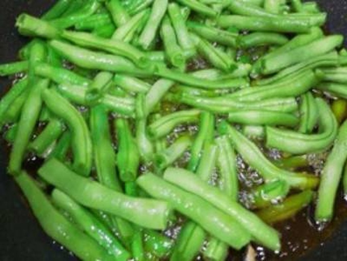 豆角在锅中被油翻炒的场景