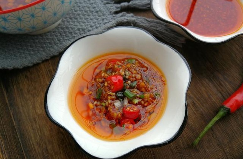 糍粑辣椒成品特写：深红油润膏体盛于白瓷碗中，表面浮一层清亮红油，用竹勺挑起呈柔韧拉丝状，可见细腻辣椒茸颗粒与微量芝麻点