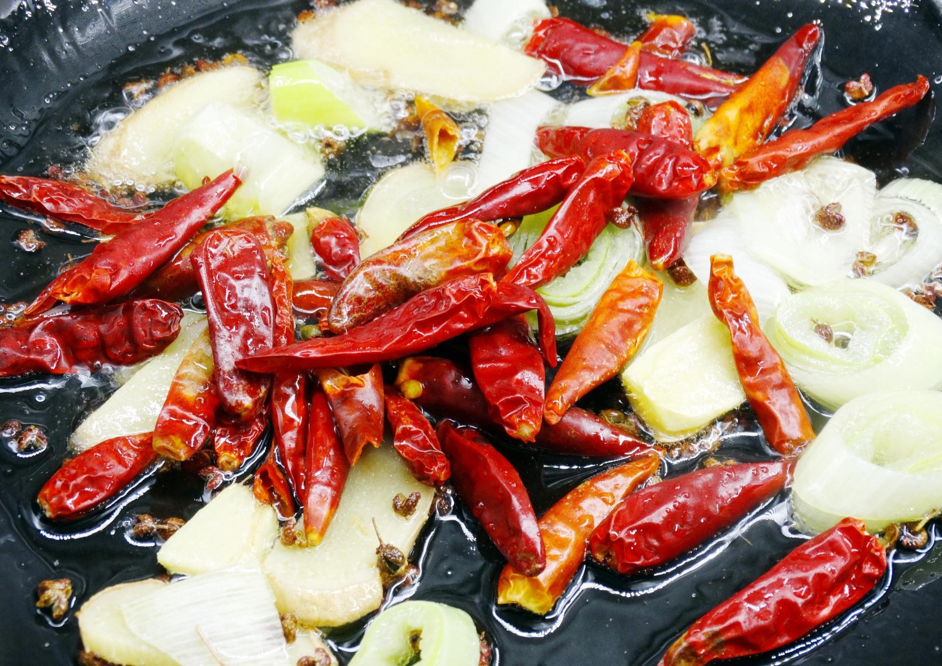 一口冒着热气的铁锅中,金黄色的蒜片与红色的羊肉片、翠绿的茼蒿正在翻炒,锅边略带焦香痕迹,体现大火快炒的烹饪技法 图片描述