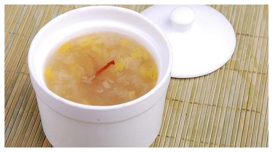 一碗乳白色清汤盛在白色瓷碗中,汤面漂浮着红色去核红枣、橙黄色姜片和少量枸杞,旁边配有一双木筷和一个小盐碟,背景为木质餐桌,整体呈现温馨家庭用餐氛围 成品红枣乌鸡汤盛出特写