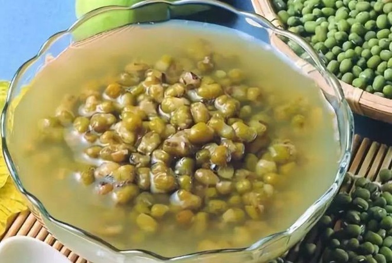 上方为一盘清炒青豌豆,豆粒饱满翠绿,搭配胡萝卜丁与蒜片,呈现清新家常风格;下方为一碗熬煮浓稠的绿豆汤,汤色碧绿转褐,表面浮有少量泡沫,旁边配有冰糖块与薄荷叶点缀,体现夏季消暑主题 青豌豆与绿豆的烹饪成品对比图