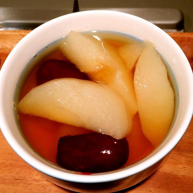 化橘红蒸雪梨成品特写：透明玻璃炖盅内盛放去核雪梨，梨心嵌入切片化橘红，汤色微黄清亮，表面浮少量细小气泡
