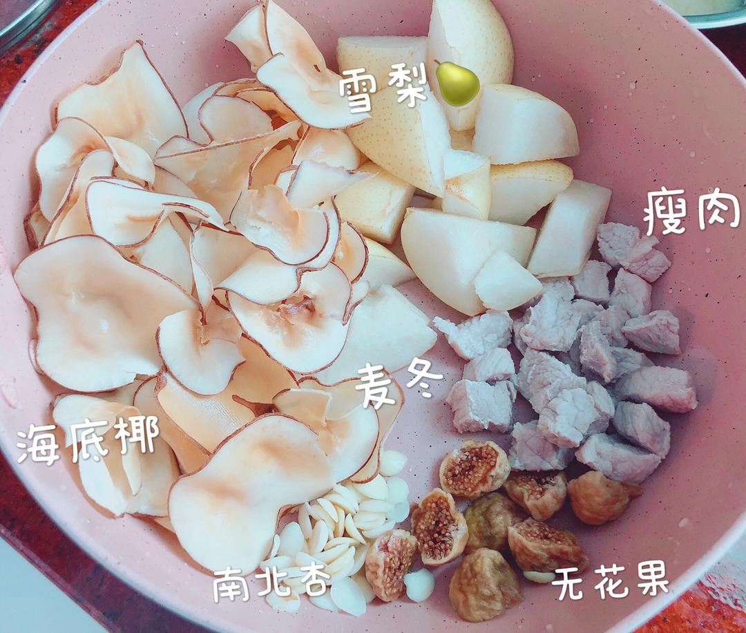 厨房操作台上摆放着多个小碗,分别装有切好的雪梨块、泡发的海底椰片、南北杏混合物、无花果干、枸杞和姜片,旁边有一盘焯过水的瘦肉块,背景可见不锈钢盆和刀具,展示雪梨海底椰煲瘦肉的完整食材准备过程 食材处理过程图