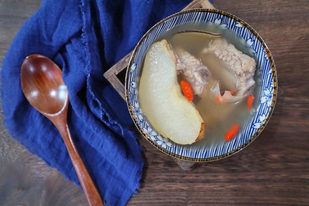 一锅热气腾腾的酸梨炖排骨,汤色清澈微黄,酸梨块与排骨交错分布,表面浮着几粒红色枸杞,旁边配有瓷勺和木筷 酸梨炖排骨成品特写
