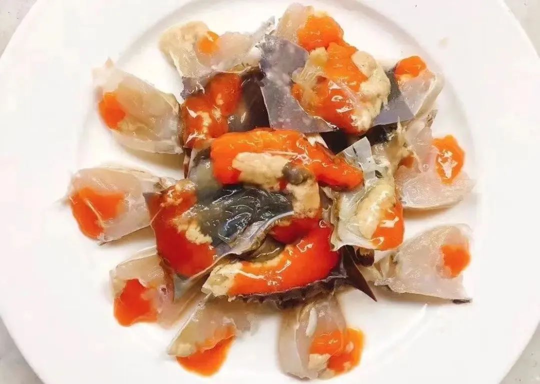 一只完整的熟制蛋黄梭子蟹,外壳呈深青褐色,打开后可见内部橙红色的蟹黄充满整个蟹体,质地油润饱满,呈现出类似咸鸭蛋黄的视觉效果,背景为木质砧板搭配绿色香草点缀,突出食材高级感 蛋黄梭子蟹特写