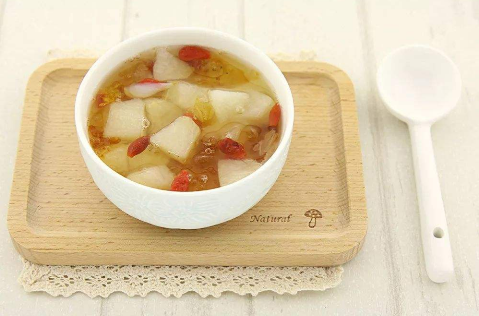 一碗金黄色的冰糖黄金梨甜瓜甜品放置在深灰色石板桌上,汤汁清澈透亮,梨片晶莹,甜瓜块鲜艳,配有银色小勺,旁边点缀一片薄荷叶,营造高级养生氛围 成品冰糖黄金梨甜瓜盛于瓷碗中