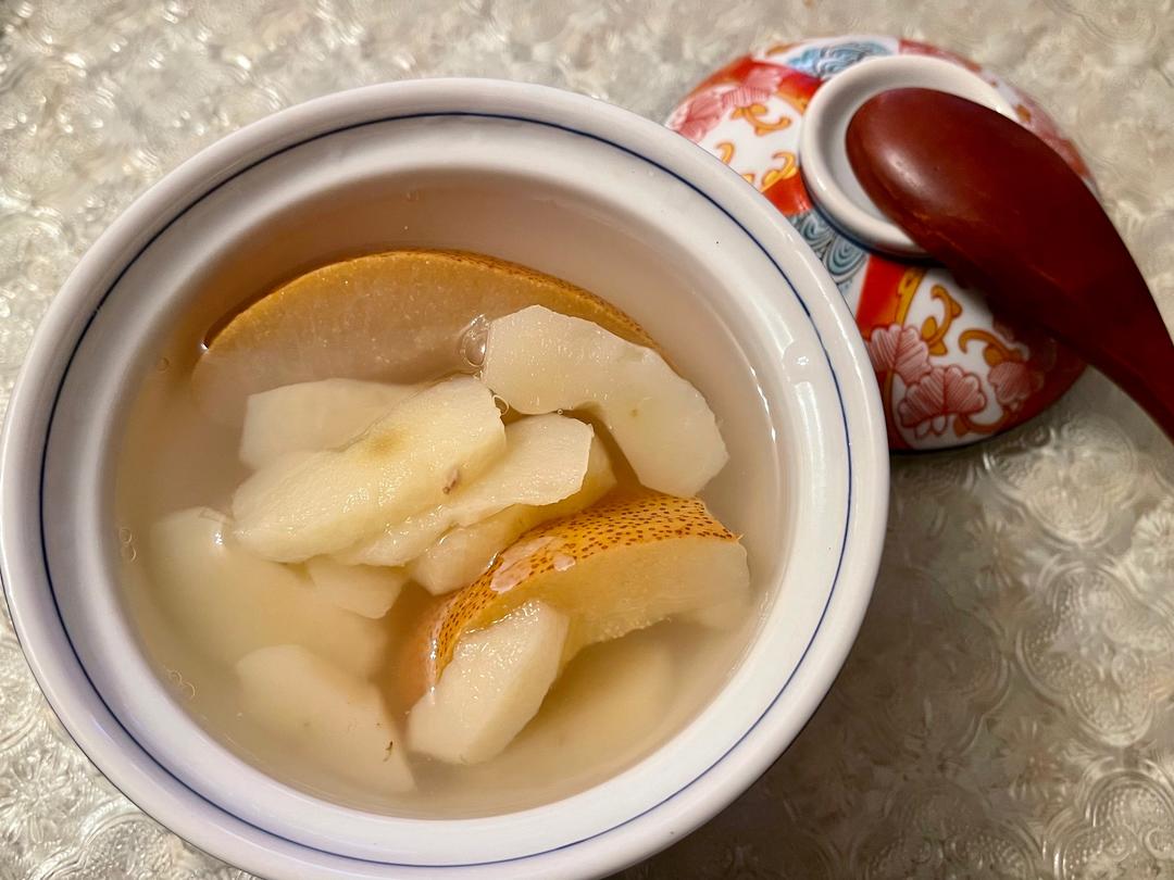 一碗刚出锅的酸梨汤盛放在白色瓷碗中,汤色清澈微黄,漂浮着几片梨肉和枸杞,热气腾腾,旁边放有一把木勺,背景为木质餐桌与秋日装饰 酸梨汤成品展示