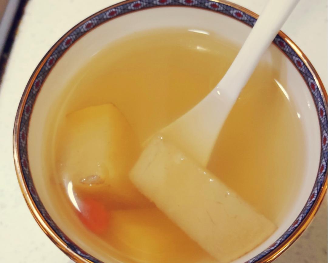 白色瓷碗中盛着一碗表面光滑的鸡蛋羹,内部均匀分布着细碎的黄色野菊花头,整体呈现淡黄绿色调,顶部点缀几滴香油,旁边摆放一双木筷 野菊花蒸蛋成品图