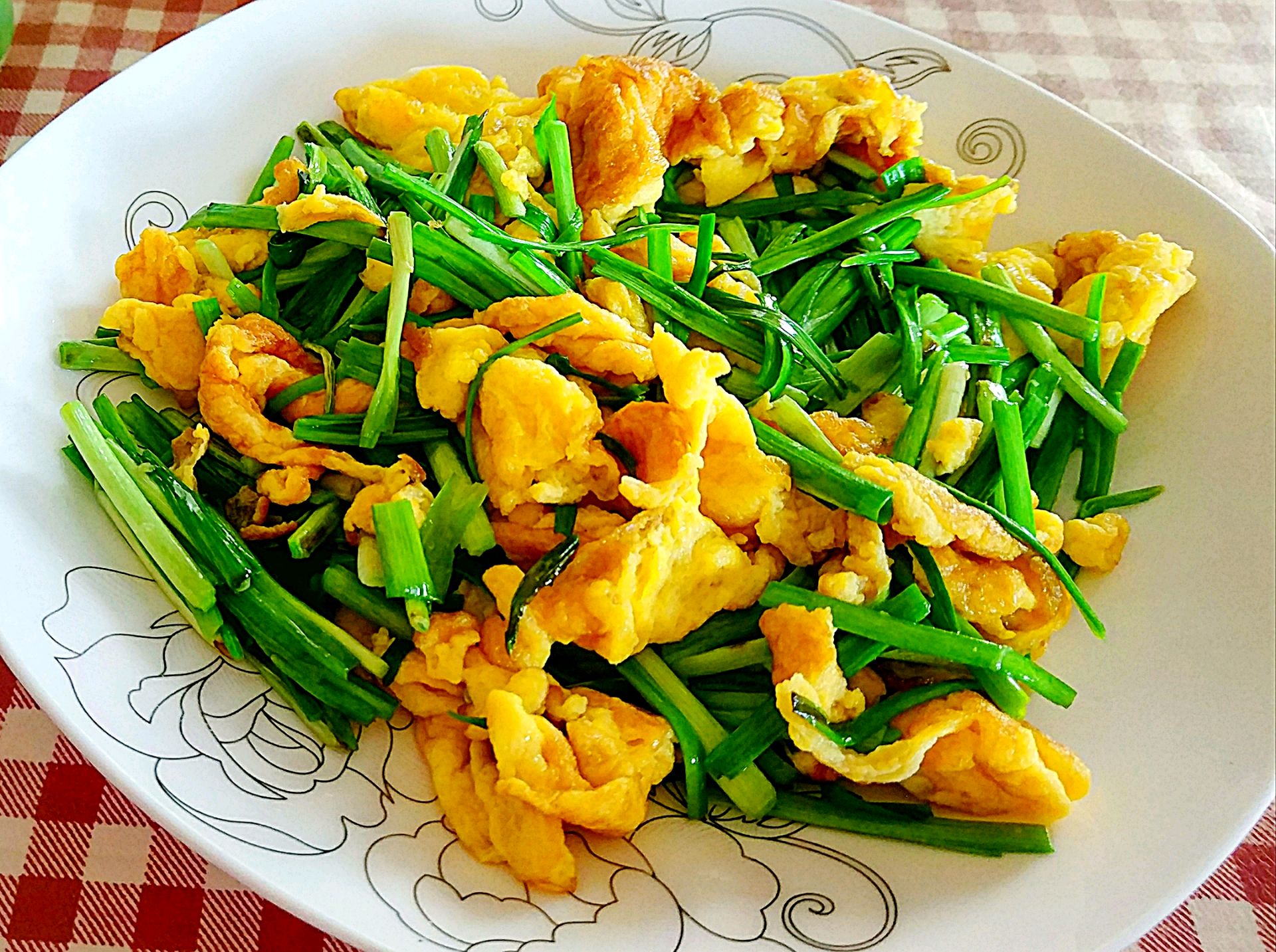 一位家庭主妇在厨房灶台前翻炒锅中的韭菜与鸡蛋,锅中食材金黄翠绿相间,热气腾腾,旁边备有切好的韭菜段和打散的鸡蛋液,展现家常健康烹饪场景 家庭厨房中制作韭菜炒鸡蛋的过程图