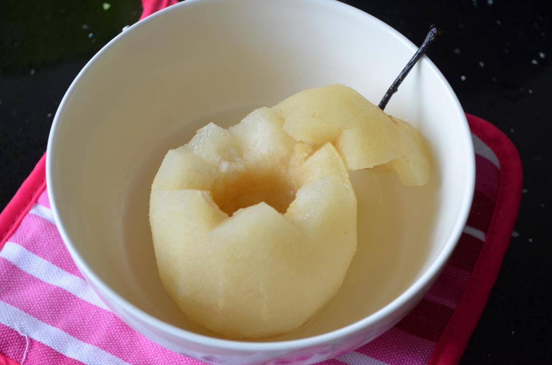 一个剖开去核的香梨放置于陶瓷烤碗中,放入家用烤箱中层,周围环绕暖黄色热光,梨肉边缘微焦,中心冒热气,旁边放有一把小勺,准备食用 家庭烤箱中正在烘烤的香梨特写