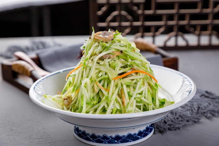 一道刚出锅的小黄瓜炒菜被盛放在圆形白瓷盘中央,菜品呈现翠绿色黄瓜片与浅褐色肉片交错分布,表面泛着光泽的薄芡,边缘点缀红椒丝和葱花,背景虚化的餐桌上有一碗米饭和一双筷子,整体风格清新自然 成品小黄瓜炒菜的高清摆盘图