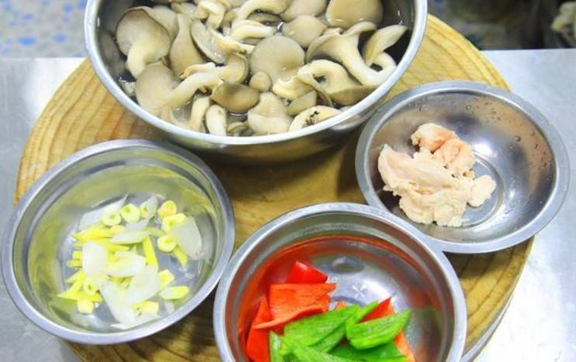 厨房操作台面上摆放着切好的白色菌菇(白玉菇和蟹味菇)、浅粉色带芽的新鲜子姜丝、剥皮大蒜瓣、红色小米辣,旁边配有量勺和调料瓶,背景为明亮自然光下的木质砧板 图片描述