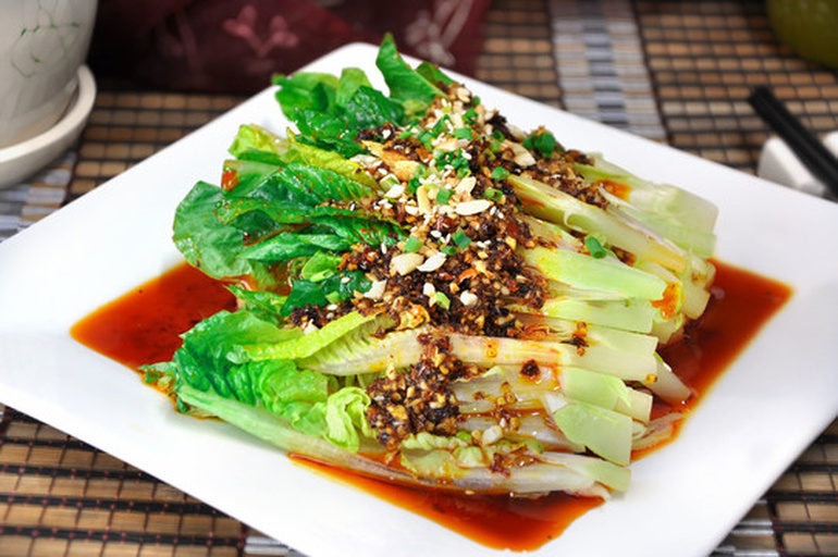 一碗调制好的红亮辣椒油与蒜末、小米辣、芝麻混合在玻璃调料碗中，旁边摆放筷子