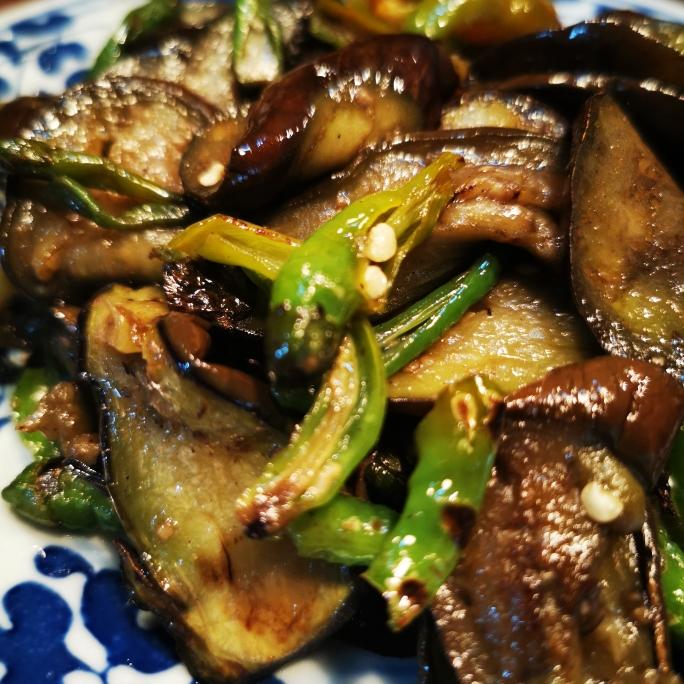 素炒长茄最终成品图:①茄片完整不碎、边缘微卷显火候 ②油亮不泛白、无水渍残留 ③青红椒色彩鲜亮、蒜粒金黄不焦 ④盘底干净无酱汁淤积 素炒长茄成品特写:油亮深紫色茄片整齐铺陈,嵌着翠绿青椒、红椒与金黄蒜粒,表面泛自然光泽无水渍,盛装于浅口青花瓷盘中,背景虚化木质餐桌
