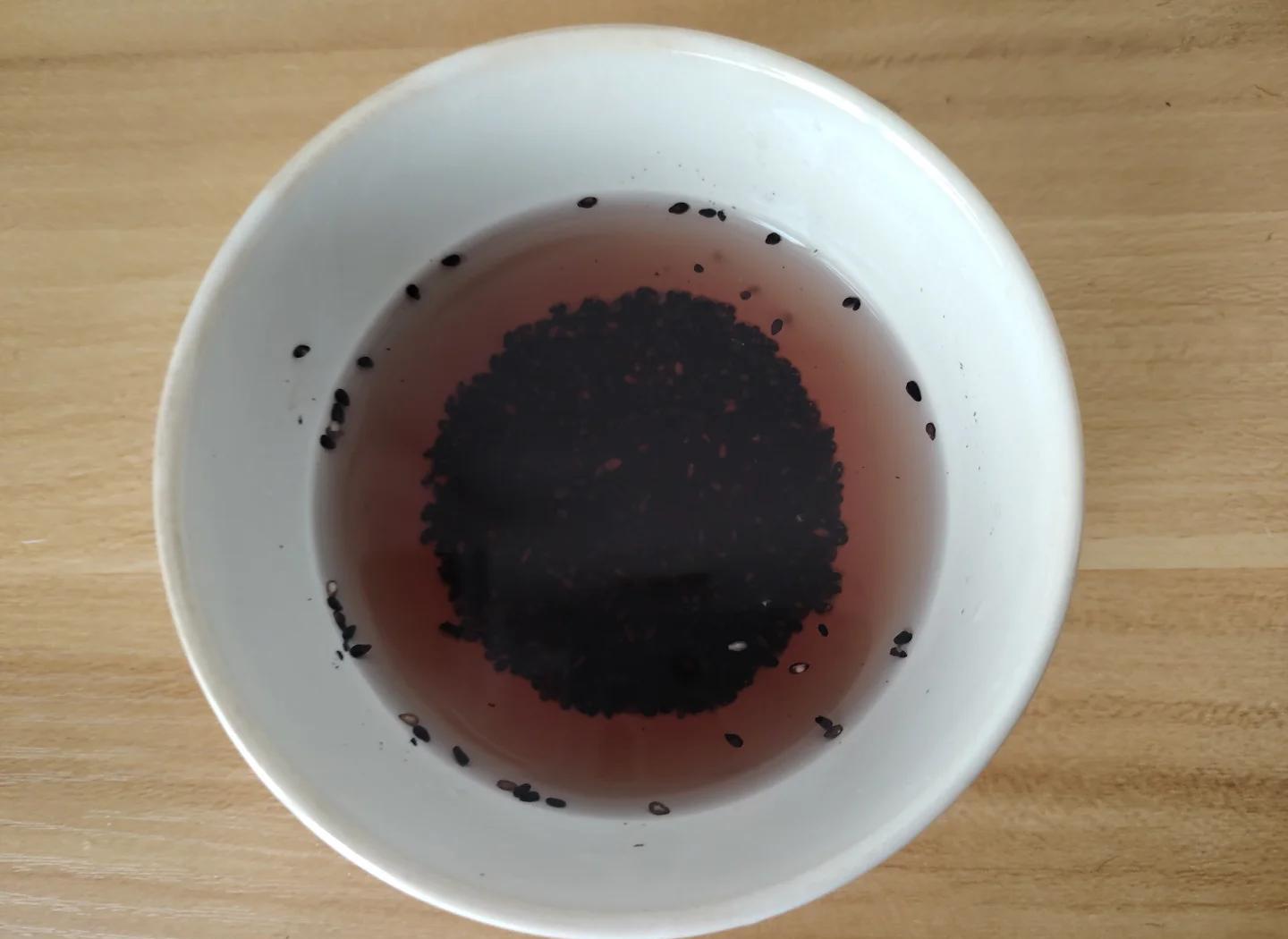 透明玻璃锅中正在蒸煮黑糯玉米,锅内水呈现淡紫色至深紫色梯度;旁边放置一碗清水对照,另一侧为三个烧杯分别装有不同浓度的浸泡液,用于展示花青素溶出过程 蒸煮过程中黑糯玉米掉色实验图