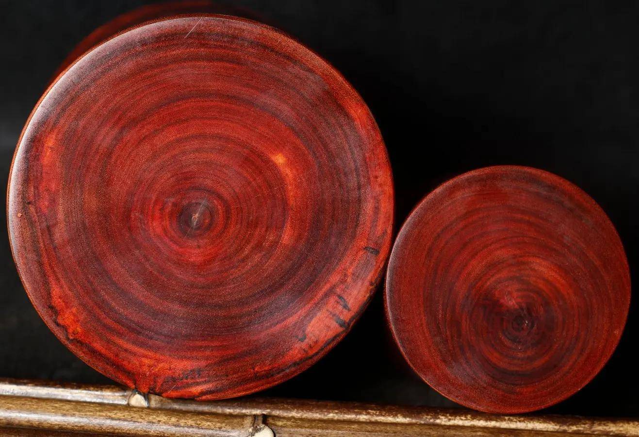 一根粗壮的非洲金花梨原木被横向锯开,露出深红褐色带金色光泽的年轮纹理,表面有自然油性反光,木质细腻,可见明显的交错纹理和矿物线分布 非洲金花梨原木剖面特写