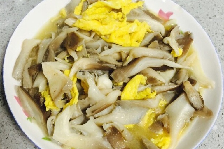 平菇炒鸡蛋烹饪完成状态 一碗金黄色的炒鸡蛋与乳白色的平菇混合翻炒在锅中,鸡蛋呈块状蓬松,平菇湿润有光泽,葱花点缀其间,热气腾腾