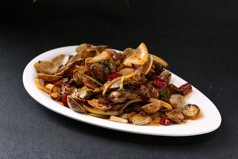 成品辣炒花蛤特写,色泽红亮,花蛤全部开口,表面裹满酱汁,搭配青红椒丝和翠绿葱花,极具食欲感 一盘红亮诱人的辣炒花蛤盛在蓝色陶瓷盘中,配以青红椒丝和葱花点缀,背景为木质餐桌