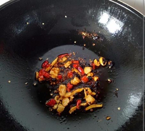 一口黑色不粘炒锅中,铲子正在翻炒翠绿色的茼蒿与金黄色虾皮的混合物,蒜末清晰可见,热气腾腾,菜肴色泽鲜亮 锅中正在翻炒茼蒿与虾皮混合物