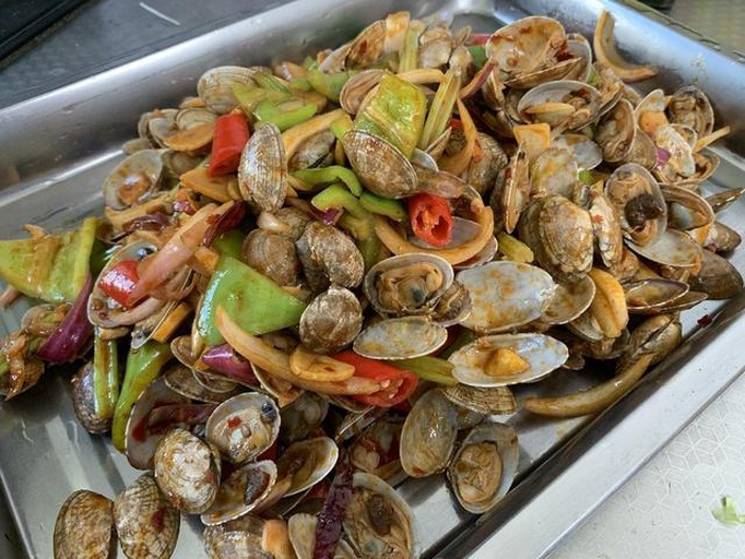 花蛤标准化焯水工艺演示:精准控制70秒沸水处理,实现嘌呤有效析出与肉质鲜嫩平衡,体现家庭可操作性 厨房场景:不锈钢锅中花蛤正在沸水中焯烫,壳已微微张开,水面浮起少量泡沫,厨师手持漏勺准备捞出,操作台摆放洗净的蒜末与香葱