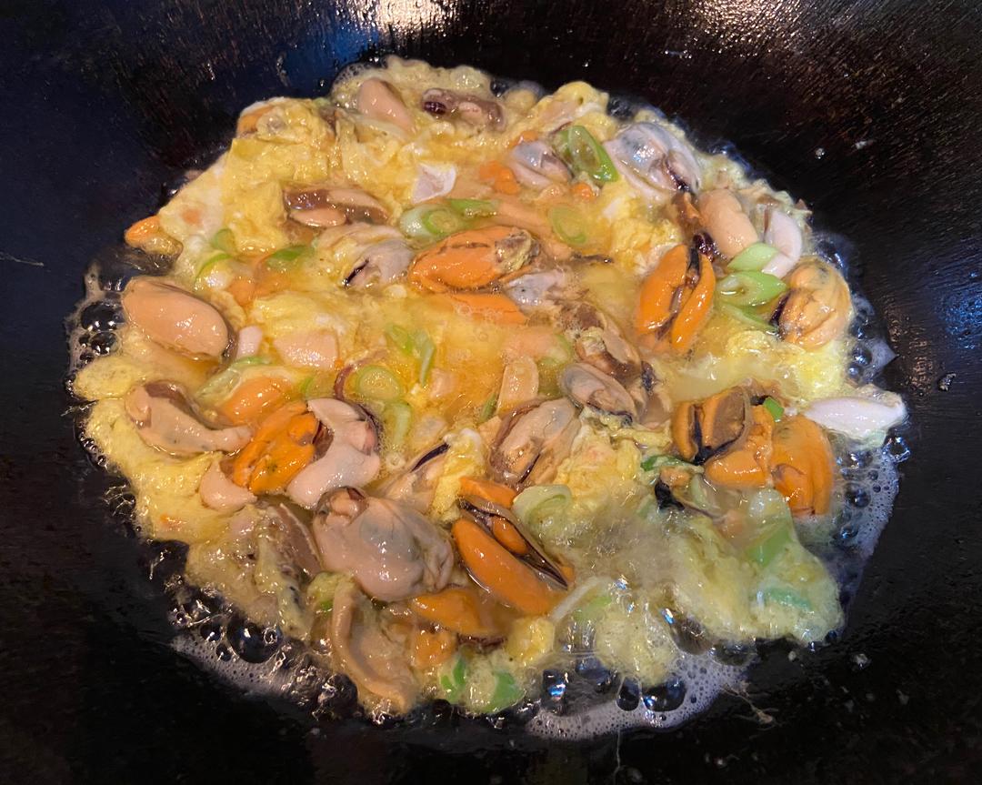 厨房操作台上正在制作福建特色海蛎煎,新鲜海蛎子倒入打散的鸡蛋液中,旁边放有葱花和地瓜粉,平底锅中油温正热,准备下锅煎制 福建海蛎煎制作过程